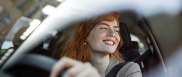 Beautiful young woman driving her new car at sunset. Woman in car. Close up portrait of pleasant looking female with glad positive expression, woman in casual wear driving a car