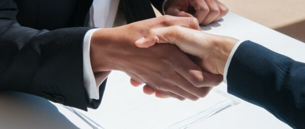 Closeup of business people shaking hands outdoors. Business man and woman wearing formal clothes and sitting at table with papers. Agreement concept.
